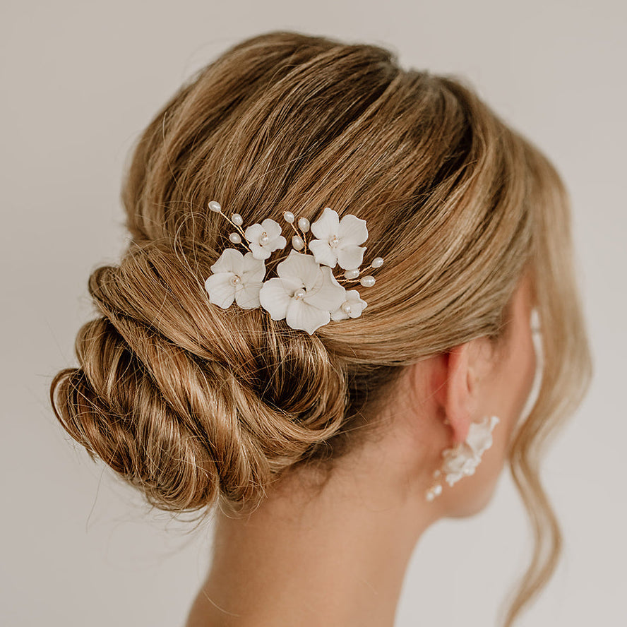 Braut Haarnadeln Coco in Gold mit weißen Porzellanblüten und echten Süßwasserperlen, getragen in einer eleganten Hochsteckfrisur
