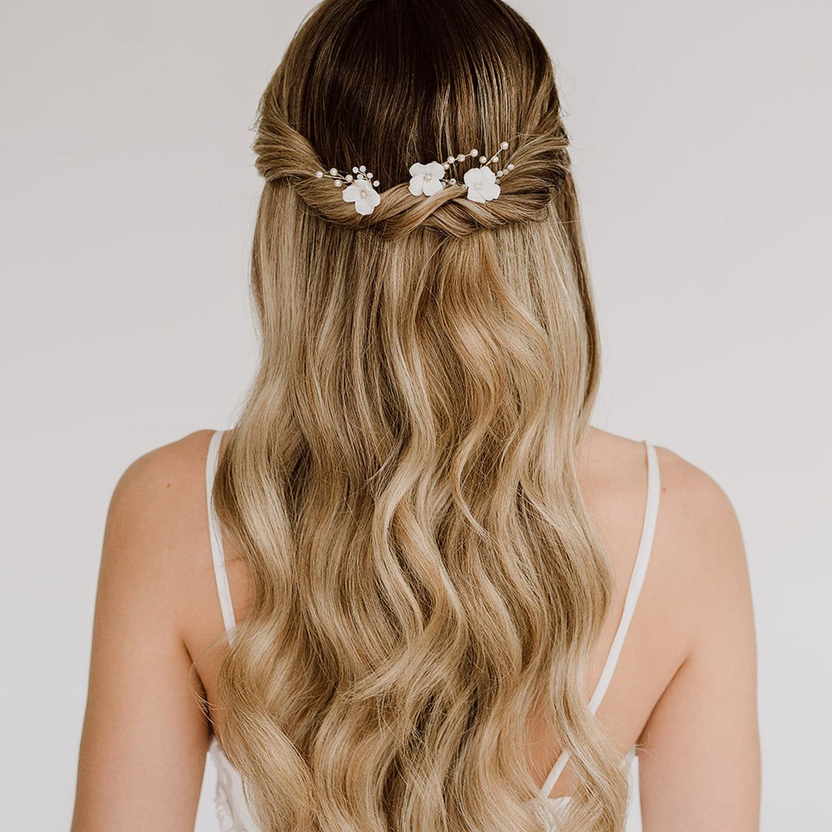 3er Set Braut Haarnadeln Coco mit weißen Porzellan Blüten und veganen Perlen in Gold, getragen von einem Model in einer halboffenen Brautfrisur