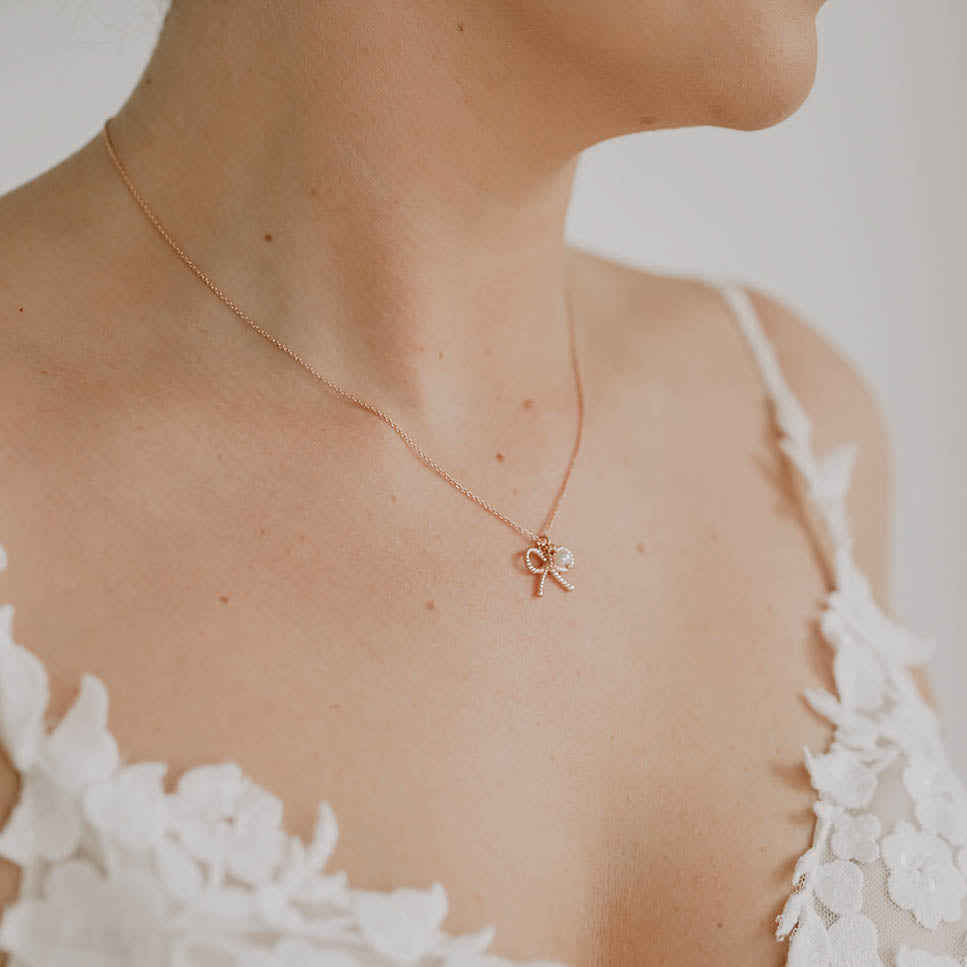 Braut Halskette Pinella aus 925 Sterlingsilber 18K rosévergoldet mit Schleife und veganer Perle, Nahaufnahme am Model getragen