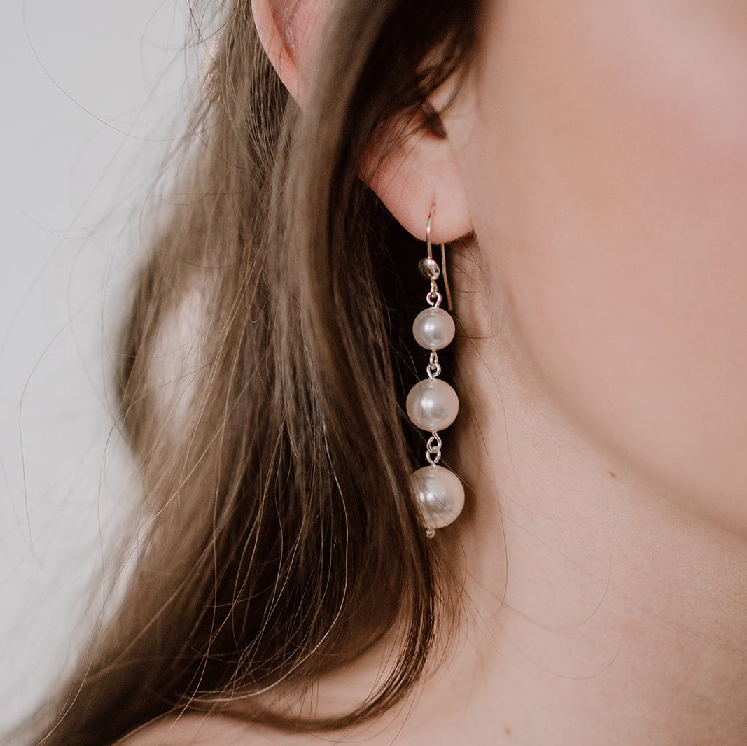 Braut Ohrringe Ida aus 925 Sterlingsilber hängend mit drei unterschiedlich großen veganen Perlen, getragen von einem Model in Nahaufnahme