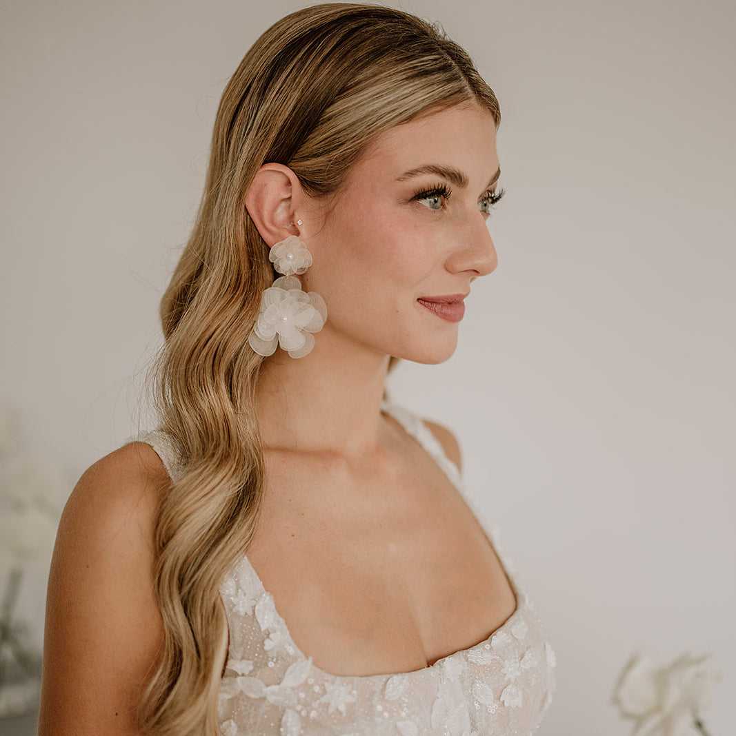 Elegante Statement Brautohrringe aus 925er Sterlingsilber 18K vergoldet mit einer großen und einer kleinen, hängenden Blüte, am Model mit spitzen Brautkleid und offenen, gewellten Haaren.