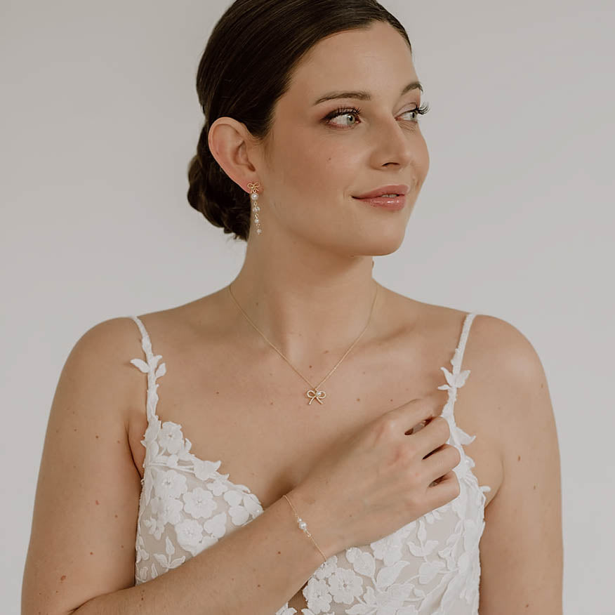 Brautohrringe Pauli mit Schleife aus 925 Sterlingsilber 18K vergoldet, darunter hängend Kristallperlen und veganer Perle, am Model getragen mit passender Schleifenhalskette Pinella und Armband Ari