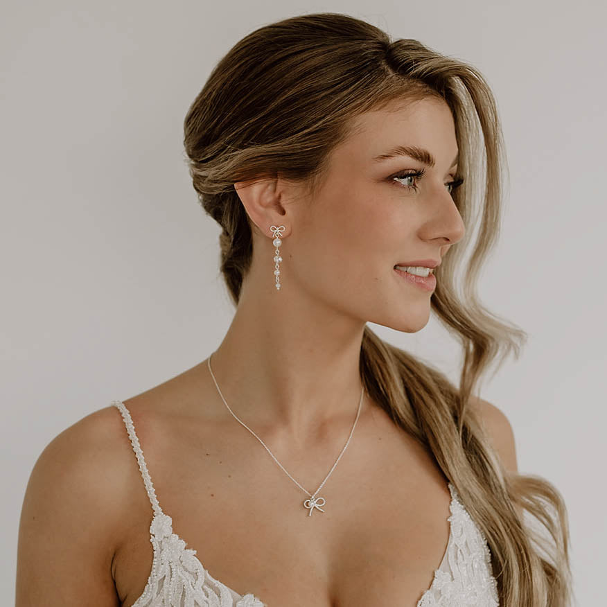 Brautohrringe Pauli mit Schleife aus 925 Sterlingsilber, darunter hängend Kristallperlen und veganer Perle, am Model getragen mit passender Schleifenhalskette Pinella