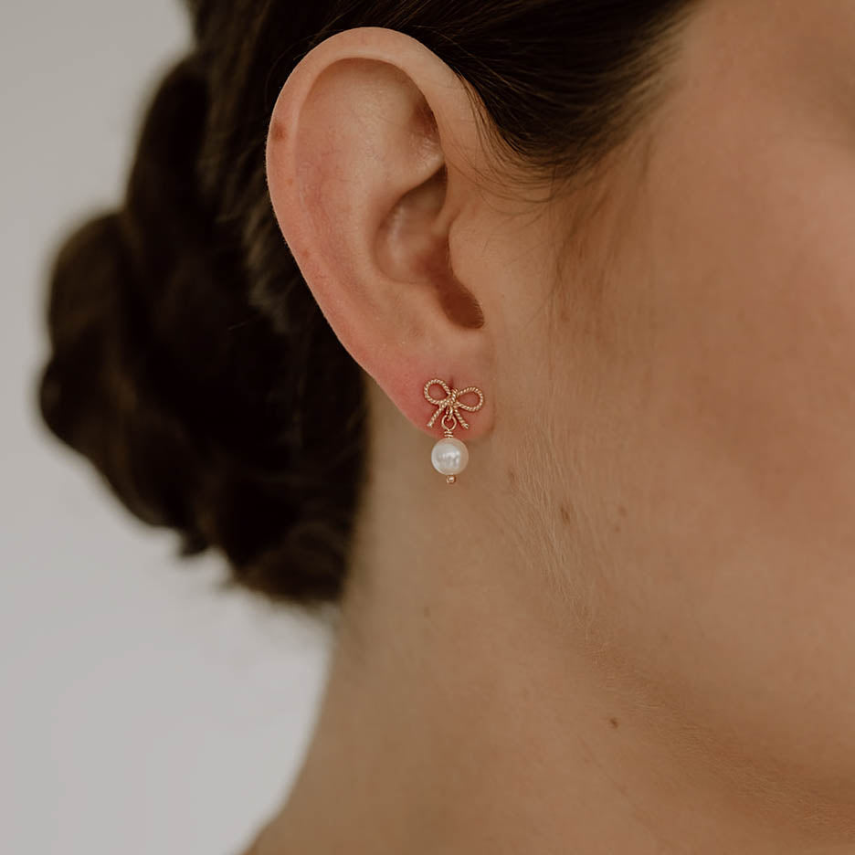 Braut Ohrringe Pinella, Schleifen Ohrstecker mit veganer Perle in 925 Sterlingsilber 18K rosévergoldet, getragen von einem Model in Nahaufnahme