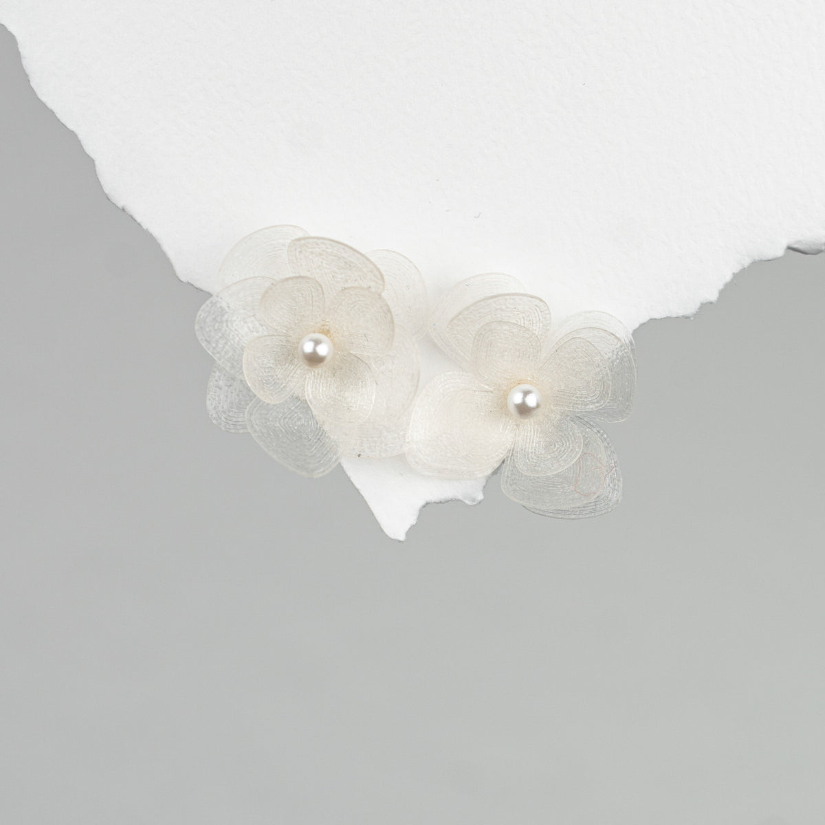 Braut Ohrstecker Carry klein aus 925 Sterlingsilber mit weißen Blüten aus biobasiertem, nachhaltigen Material und veganer Perle, liegend auf Marmorplatte