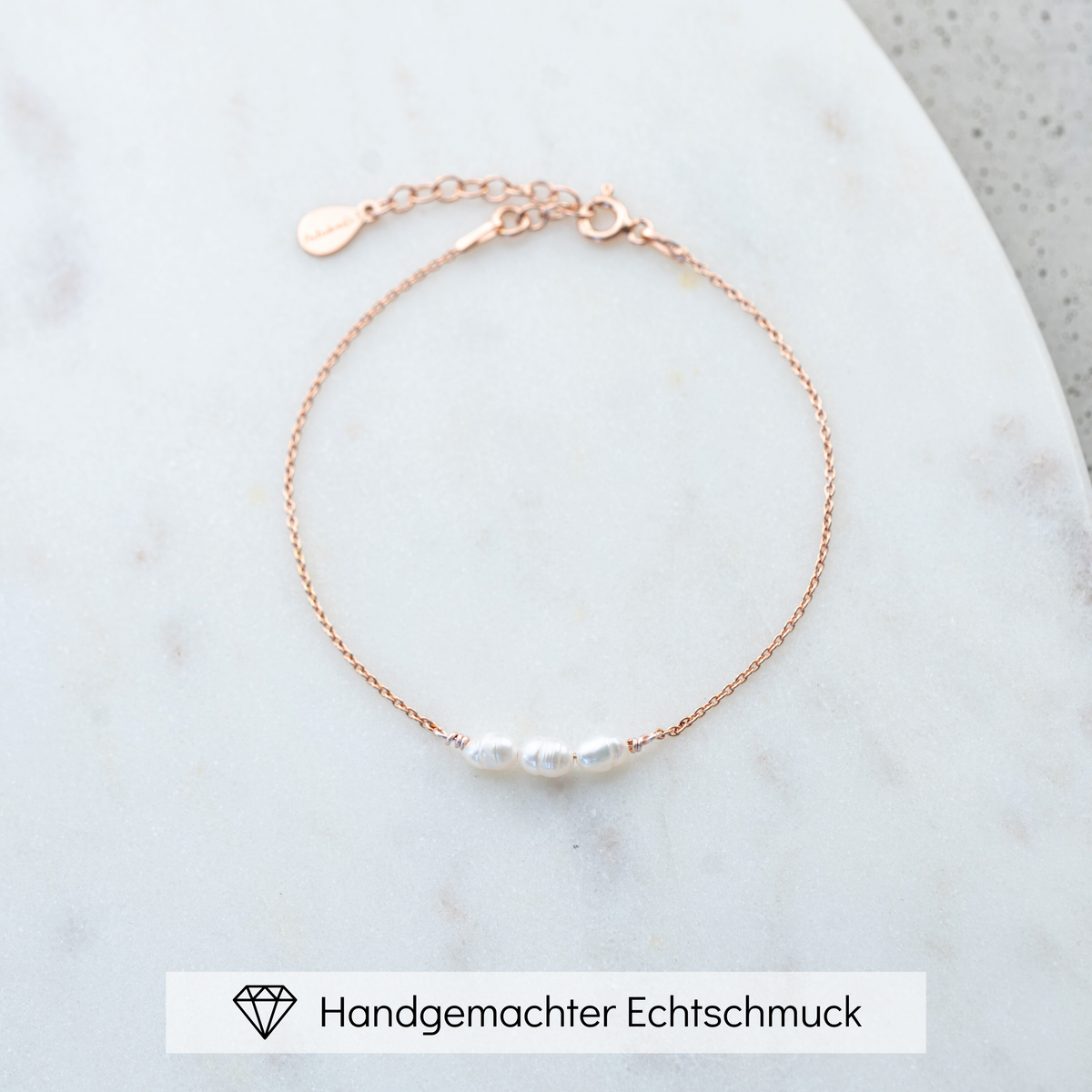 Brautarmband Amelie aus 925 Sterlingsilber 18K vergoldet mit kleinen echten Süßwasserperlen, liegend auf Marmorplatte