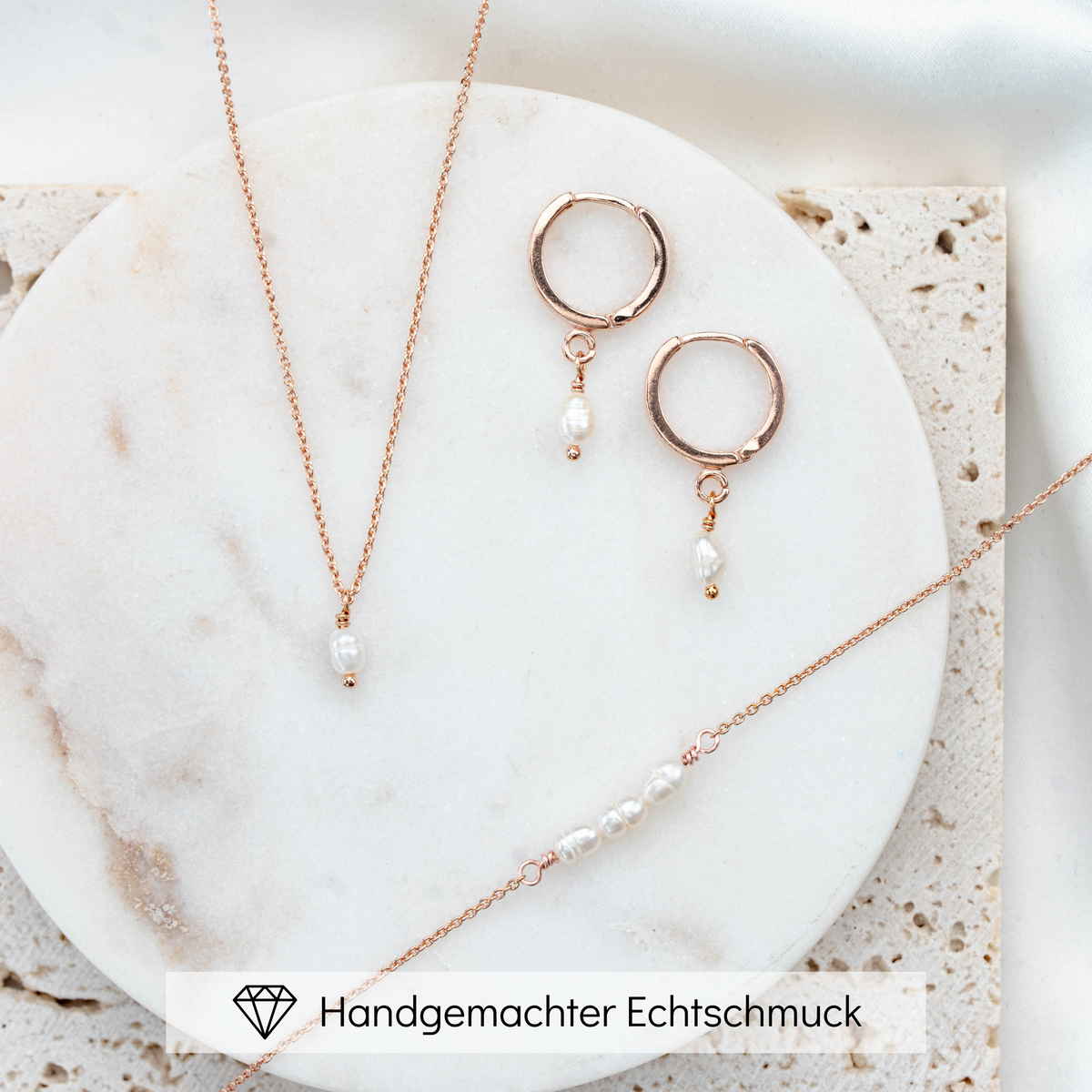 3-teiliges Brautschmuckset Amelie aus 925 Sterlingsilber 18K rosévergoldet – Creolen, Halskette und Armband mit echten Süßwasserperlen, liegend auf Marmorplatte