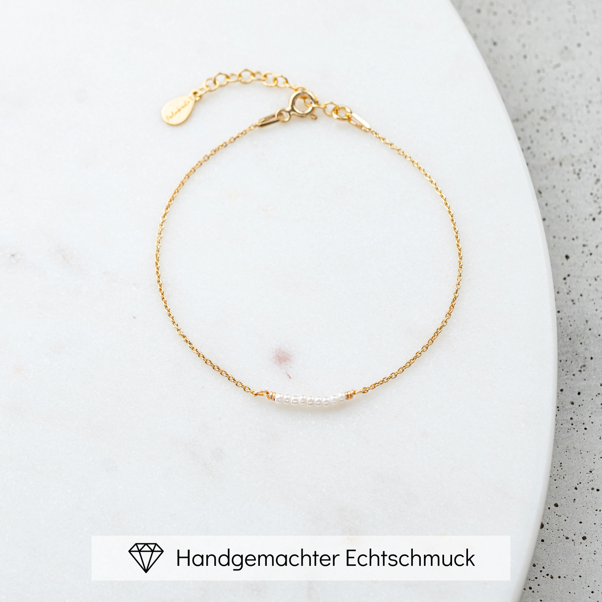 Brautarmband Belina aus 925 Sterlingsilber 18K vergoldet mit kleinen Perlen, mittig am Armband, liegend auf einer Marmorplatte