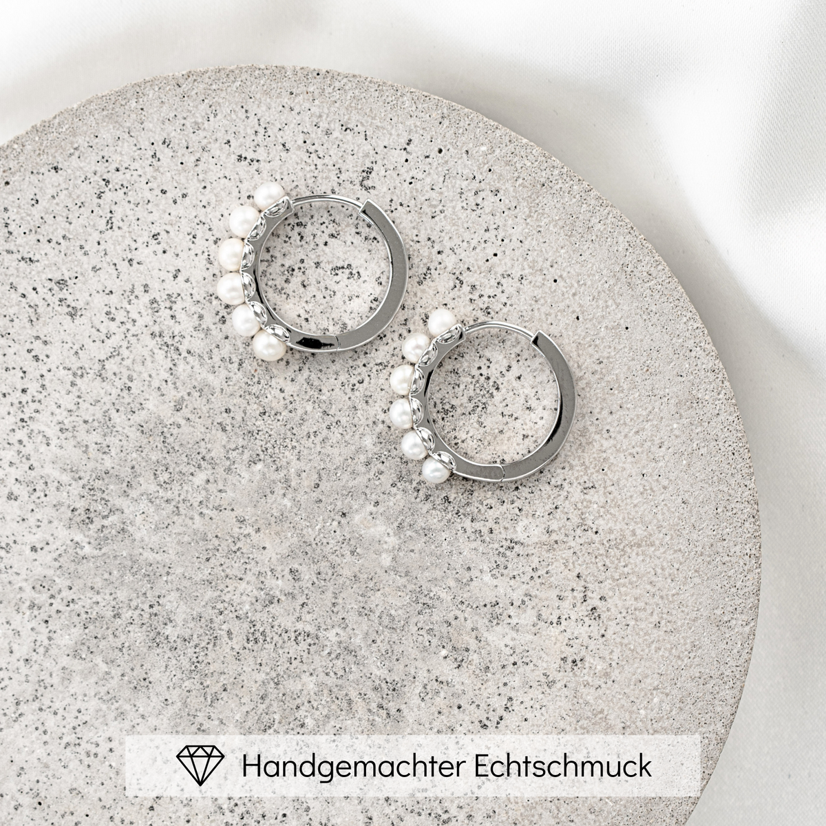 Creolen Elli aus 925 Sterlingsilber mit kleinen Süßwasserperlen, handgefertigt, liegend auf einer Betonplatte