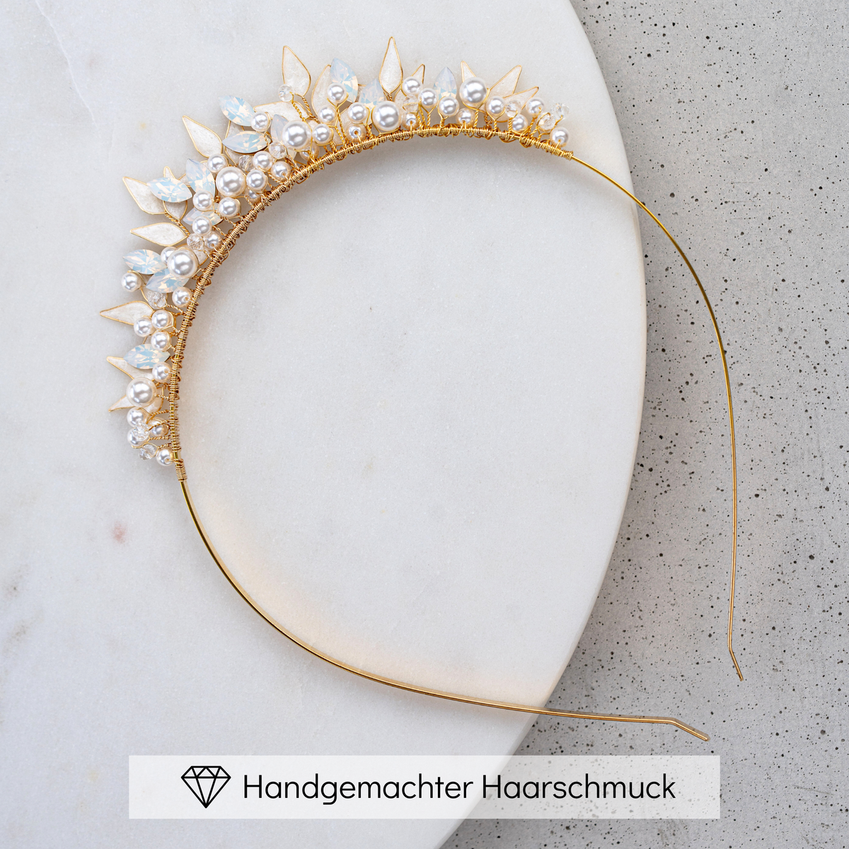 Braut Diadem Krone Greta in Gold mit veganen Perlen, white opal Kristallen und ivory farbenen Blättern, liegend auf einer Marmorplatte