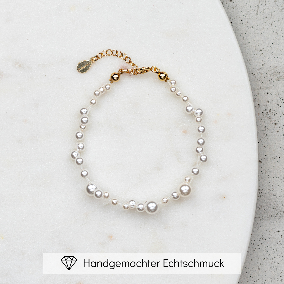 Brautarmband Jasmin mit schwebenden veganen Perlen unterschiedlicher Größe und 925er Sterlingsilber 18K vergoldetem Verschluss, liegend auf Marmorplatte