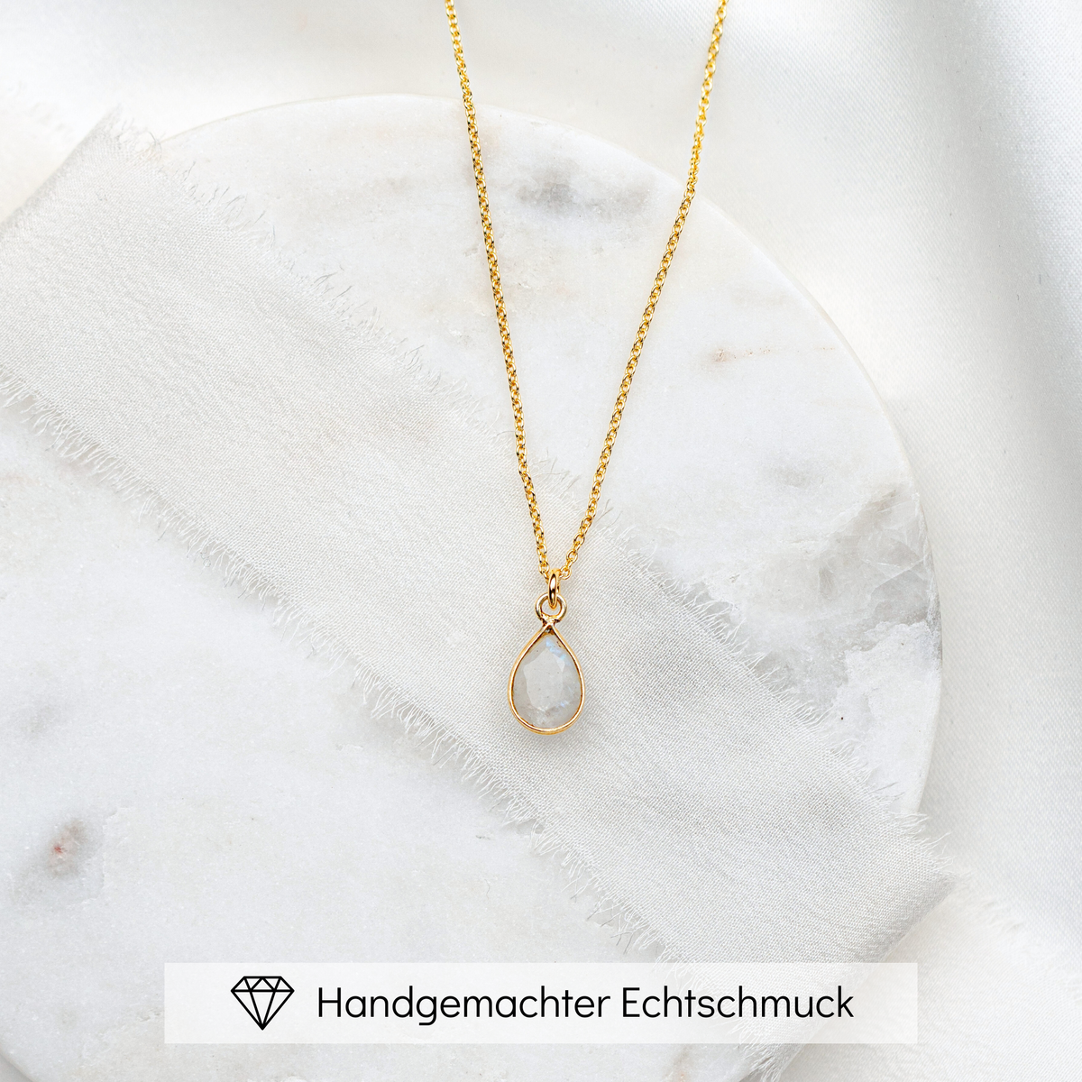 Braut Halskette aus 925er Sterlingsilber 18K vergoldet mit feiner Gliederkette und tropfenförmigem Mondstein Anhänger, präsentiert auf einer runden, hellgrauen Betonplatte
