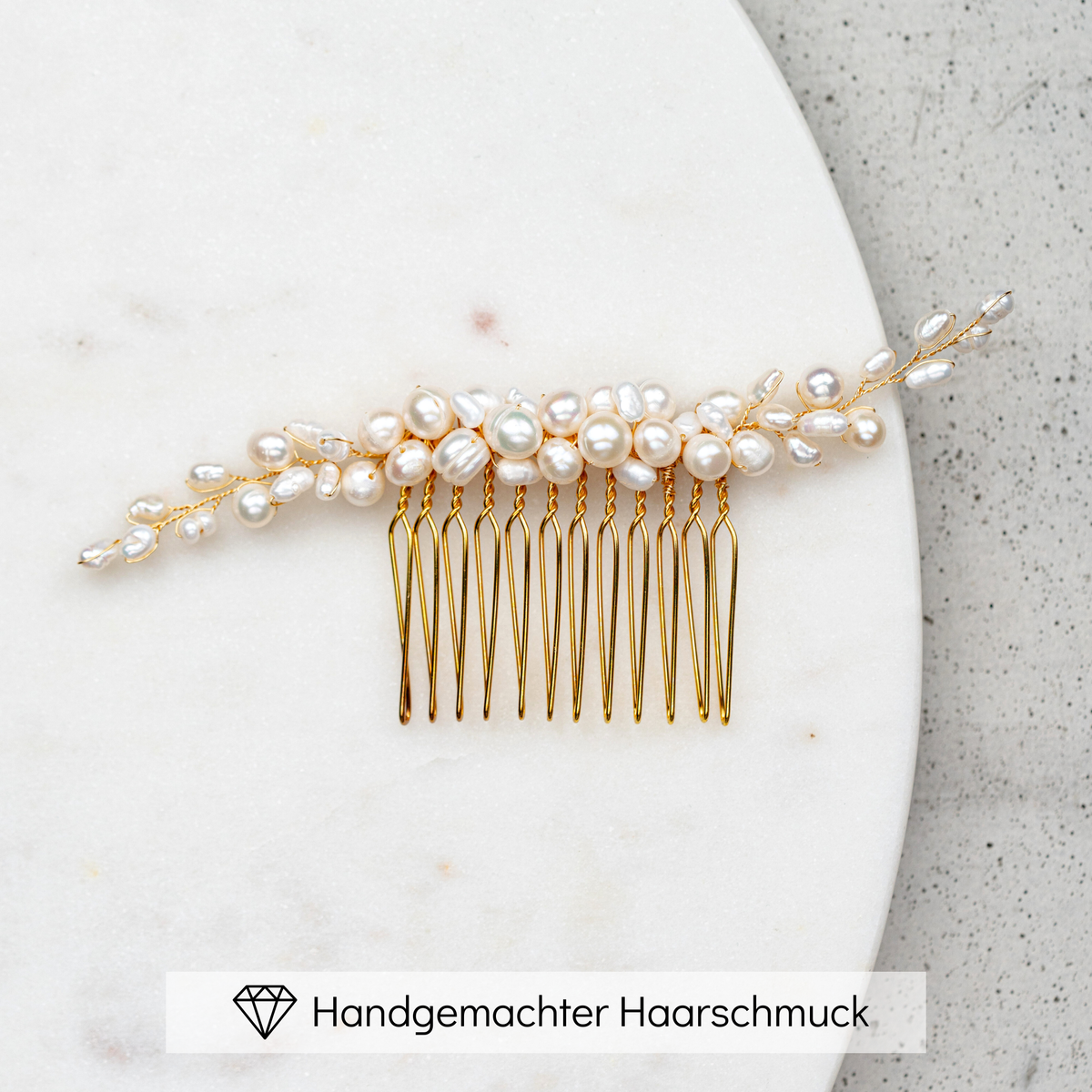 Braut Haarkamm Linda-Amelie in Gold mit unterschiedlich großen, echten Perlen, liegend auf Marmorplatte