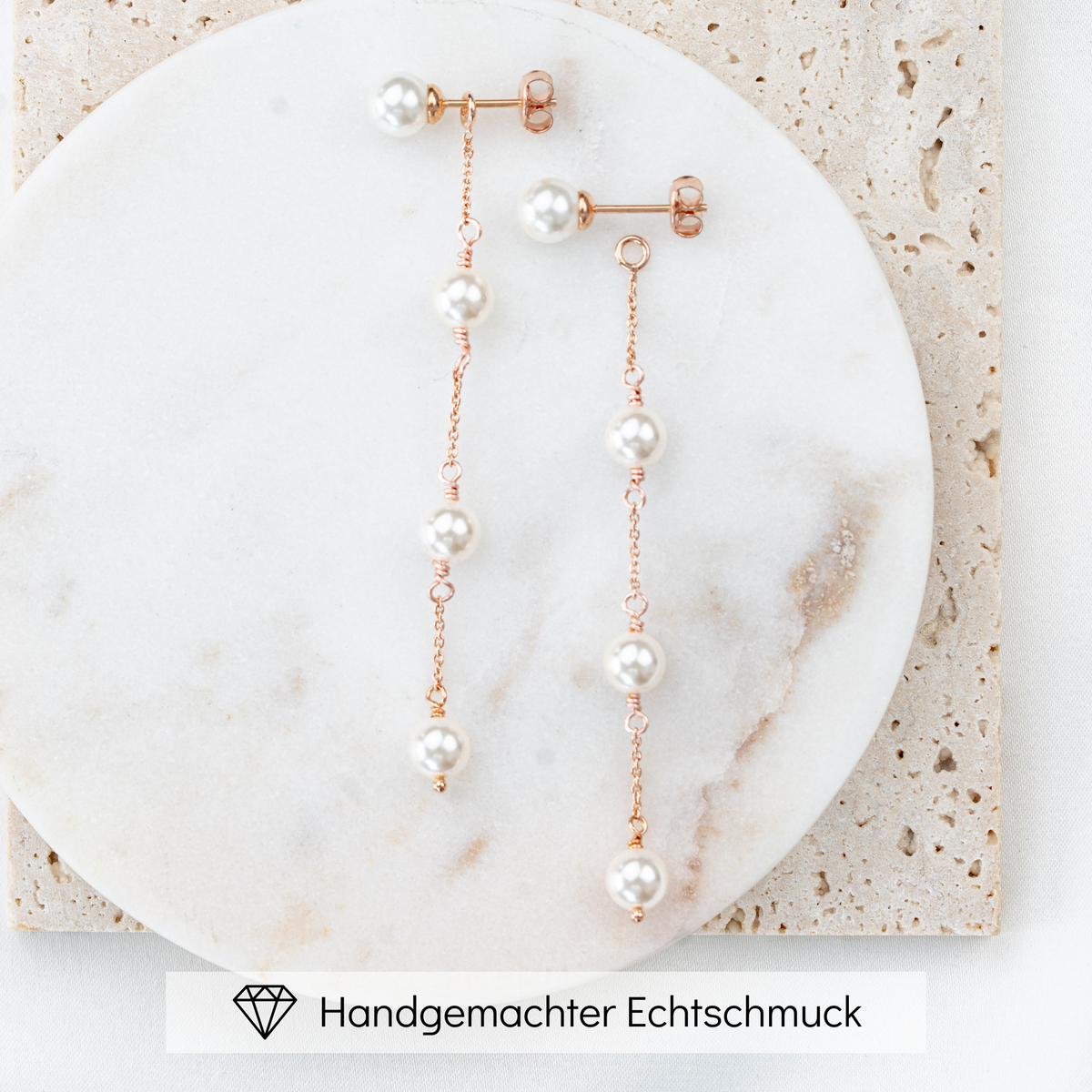 Zarte hängende Brautohrringe aus 925er Sterlingsilber 18K rosévergoldet mit rundem Perlenstecker und darunter in Reihe angeordneten, veganen, runden Perlen, verbunden mit einem feinen Kettchen, liegend auf einer hellen Marmorplatte. Der Perlenohrstecker ist abnehmbar und einzeln tragbar als schlichter Perlenstecker.
