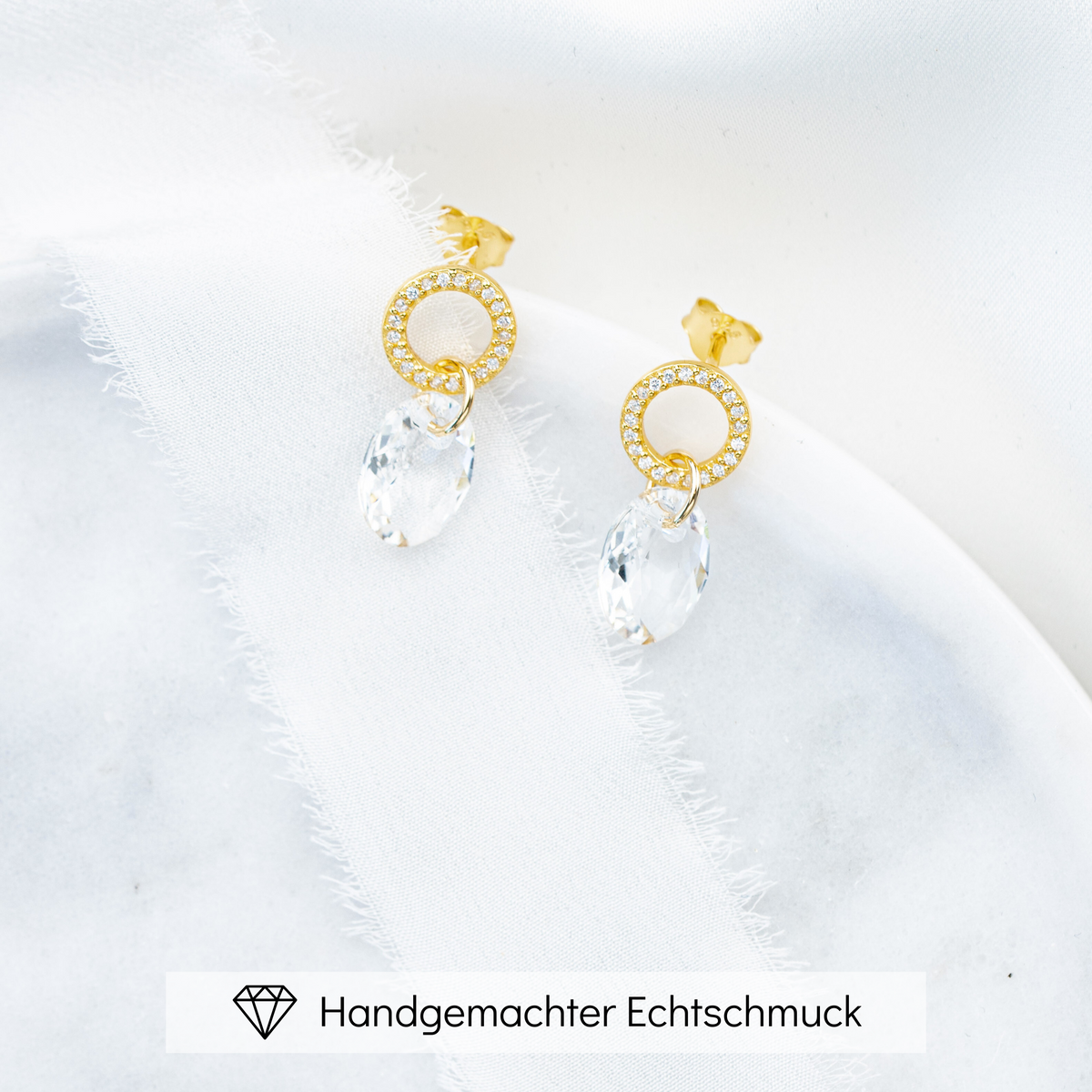 Hängender Braut Ohrring Mimi aus 925 Sterlingsilber 18K vergoldet mit Zirkonia Kristallen und facettiertem Kristall, liegend auf einer Marmorplatte