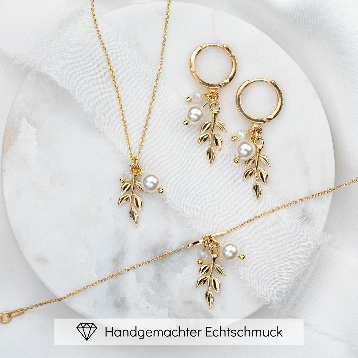 3-teiliges Schmuckset in 925er Silber 18K vergoldet bestehend aus Halskette, Creolen und Armband mit filigranen Blattanhängern, kleinen weißen Perlen und white opal Kristallperlen arrangiert auf hellem Marmorhintergrund