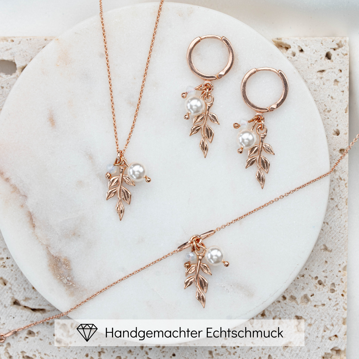 3-teiliges Schmuckset in 925er Silber 18K rosévergoldet bestehend aus Halskette, Creolen und Armband mit filigranen Blattanhängern, kleinen weißen Perlen und white opal Kristallperlen arrangiert auf hellem Marmorhintergrund