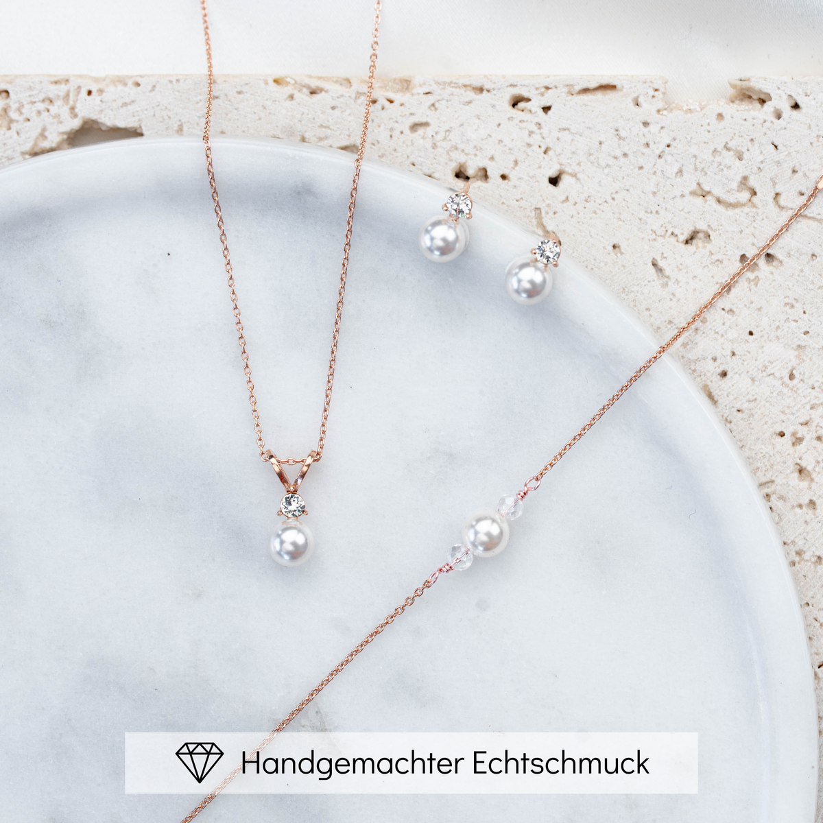 Hochwertiges Brautschmuck-Set aus 925er Sterlingsilber 18K rosévergoldet bestehend aus Brauthalskette, Ohrsteckern und Armband mit funkelndem Zirkonia Kristall und veganer Perle, ästhetisch arrangiert auf einer hellen Marmorplatte.