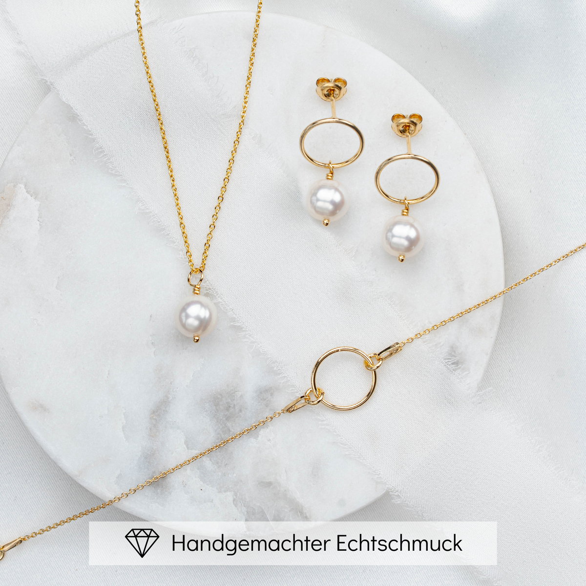 3-teiliges klassisches Brautschmuckset Toni aus 925 Sterlingsilber 18K vergoldet – Ohrringe und Halskette mit echten Süßwasserperlen, Armband mit rundem Element als Mittelteil ohne Perle, liegend auf Marmorplatte
