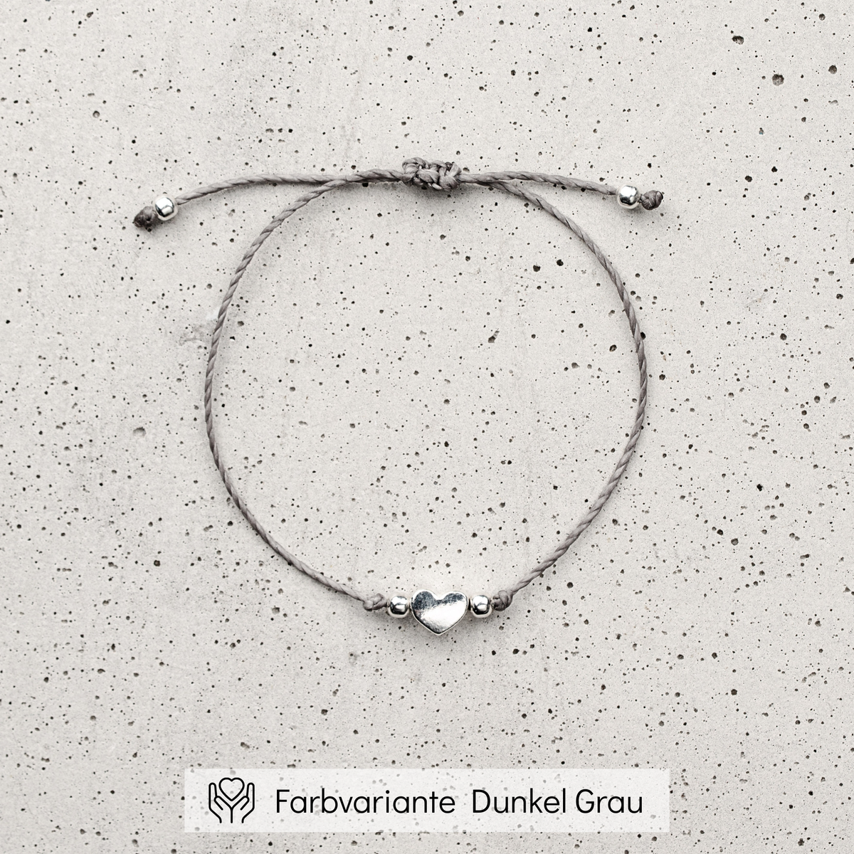 Trauzeugin Armband aus grauem Makramee-Band mit silbernem Herz-Bead, liegend auf Betonplatte
