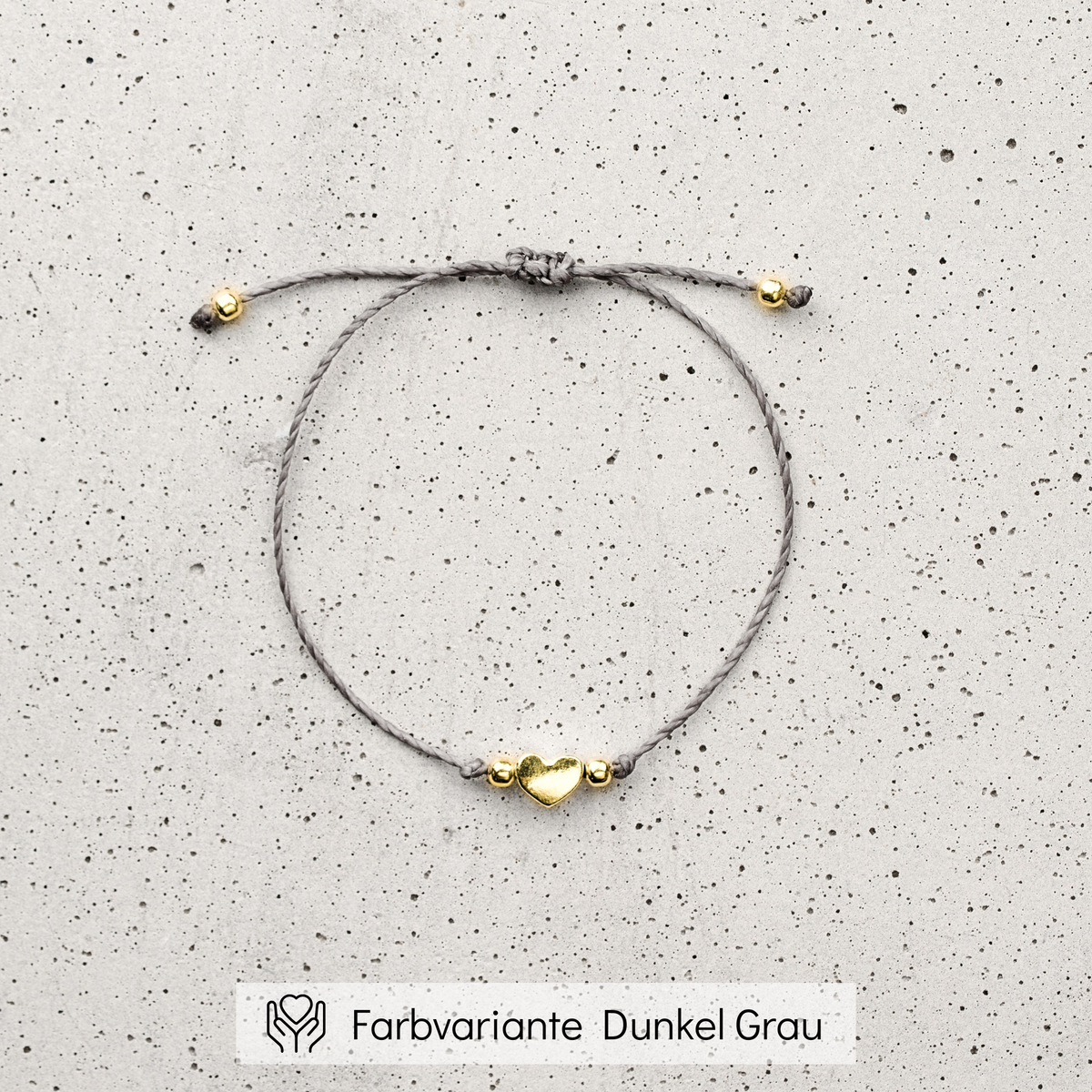 Trauzeugin Armband aus grauem Makramee-Band mit goldenem Herz-Bead, liegend auf Betonplatte