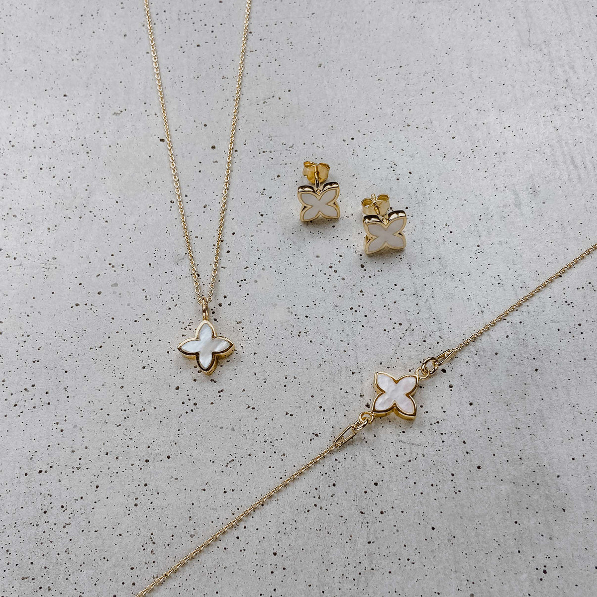 Brautset Daisy aus 925 Sterlingsilber 18K vergoldet mit kleinen perlmuttfarbenen Blüten, liegend auf einer Betonplatte