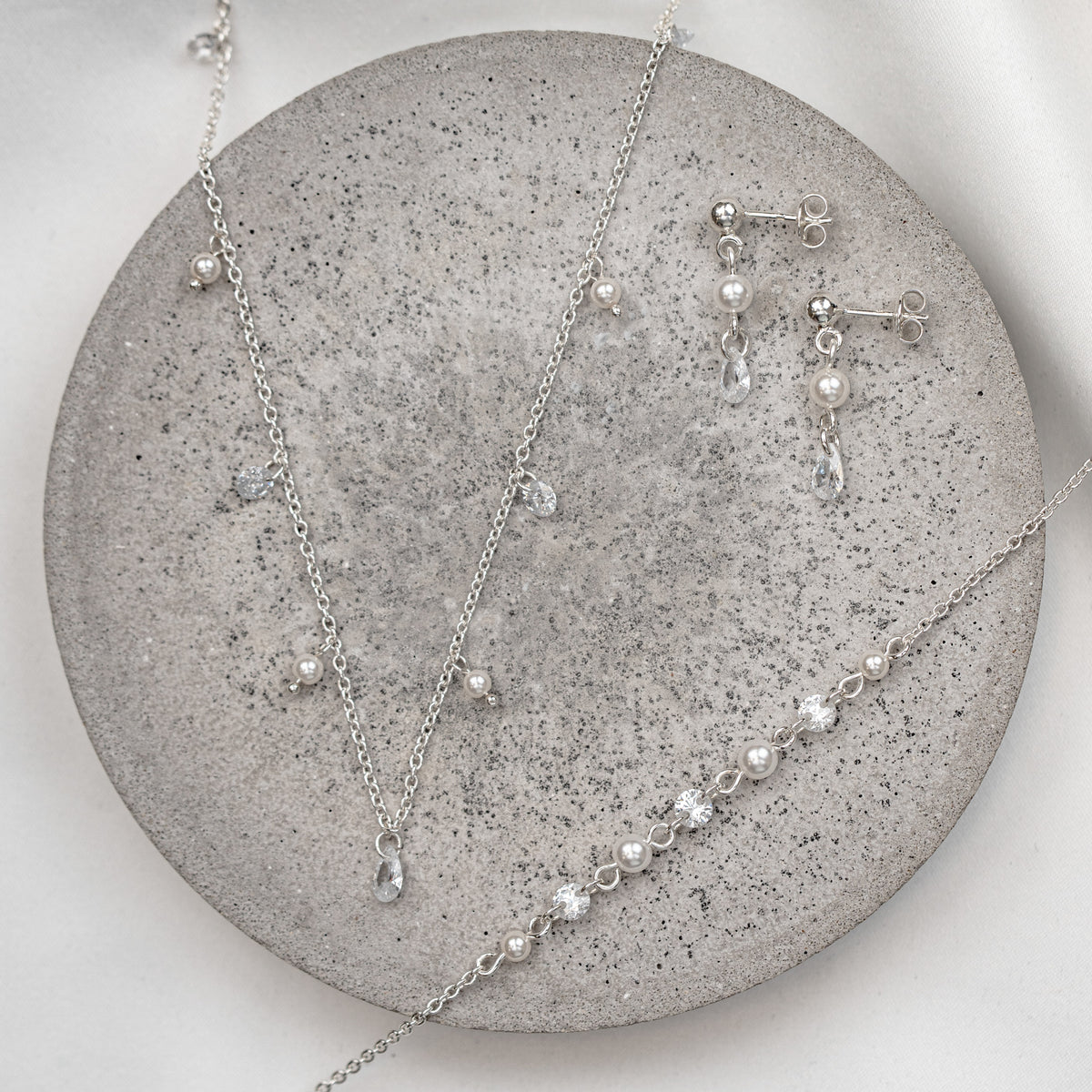 3-teiliges Brautschmuckset Amina aus 925 Sterlingsilber  – Ohrringe, Halskette und Armband mit veganen Perlen und Kristallen im Wechsel, liegend auf Marmorplatte