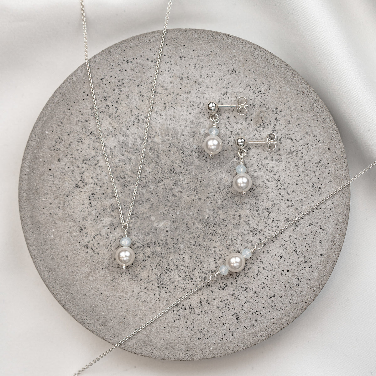 3-teiliges Brautschmuckset Ari aus 925 Sterlingsilber  – Ohrringe, Halskette und Armband mit veganen Perlen und Kristallperlen white opal, auf Marmorplatte