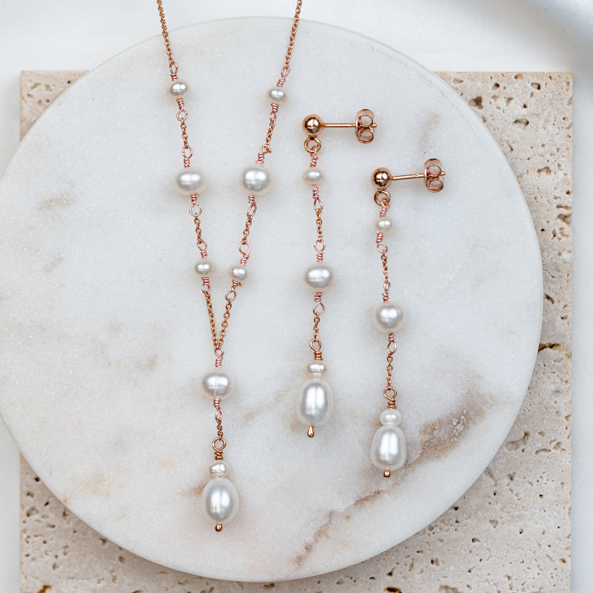 2-teiliges Brautschmuckset Joy aus 925 Sterlingsilber 18K rosévergoldet – Y-Halskette und hängende Ohrringe mit echten, unterschiedlich großen Süßwasserperlen, auf Marmorplatte