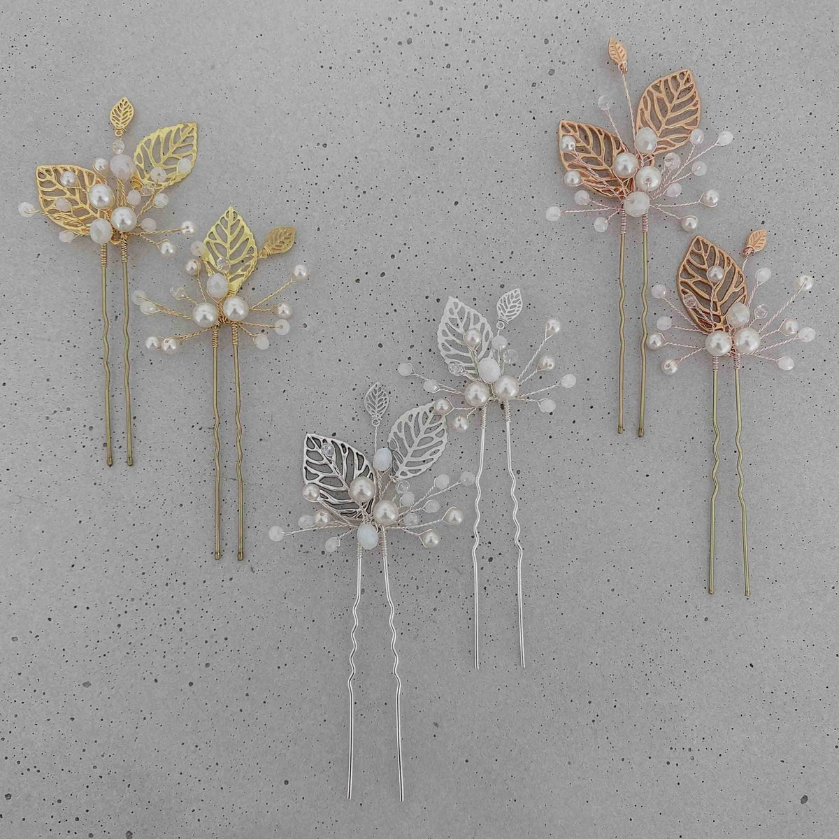 2er Set Braut Haarnadeln Zoe in Gold, Silber und Roségold mit filigranen Blättern, veganen Perlen und white opal Kristallperlen, liegend auf einer Betonplatte